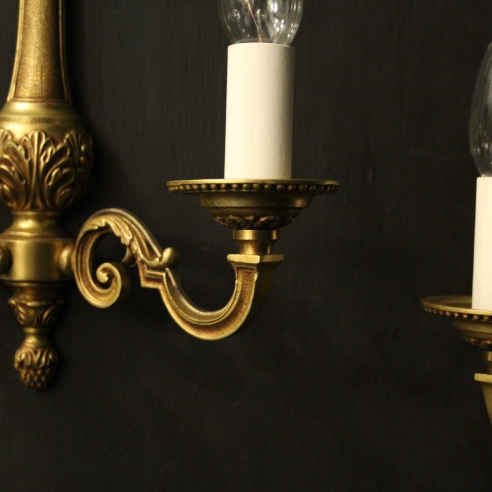 A set of four French gilded brass twin-arm wall sconces featuring scrolled arms, leaf motifs, and flame finials. View IV