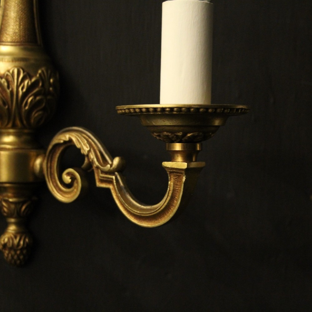 A set of four French gilded brass twin-arm wall sconces featuring scrolled arms, leaf motifs, and flame finials. View V