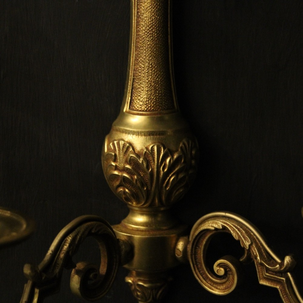 A set of four French gilded brass twin-arm wall sconces featuring scrolled arms, leaf motifs, and flame finials. View IX