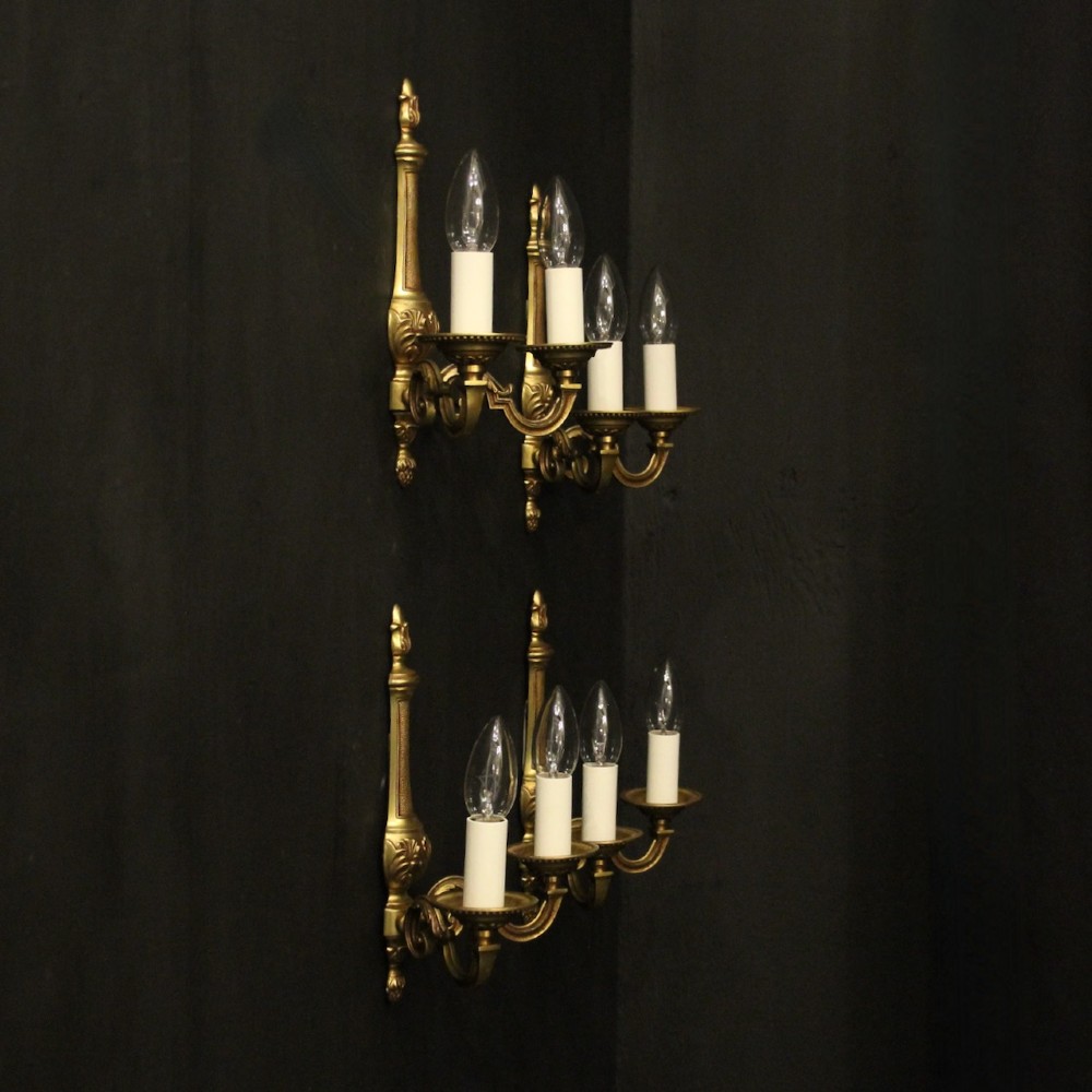 A set of four French gilded brass twin-arm wall sconces featuring scrolled arms, leaf motifs, and flame finials. View X