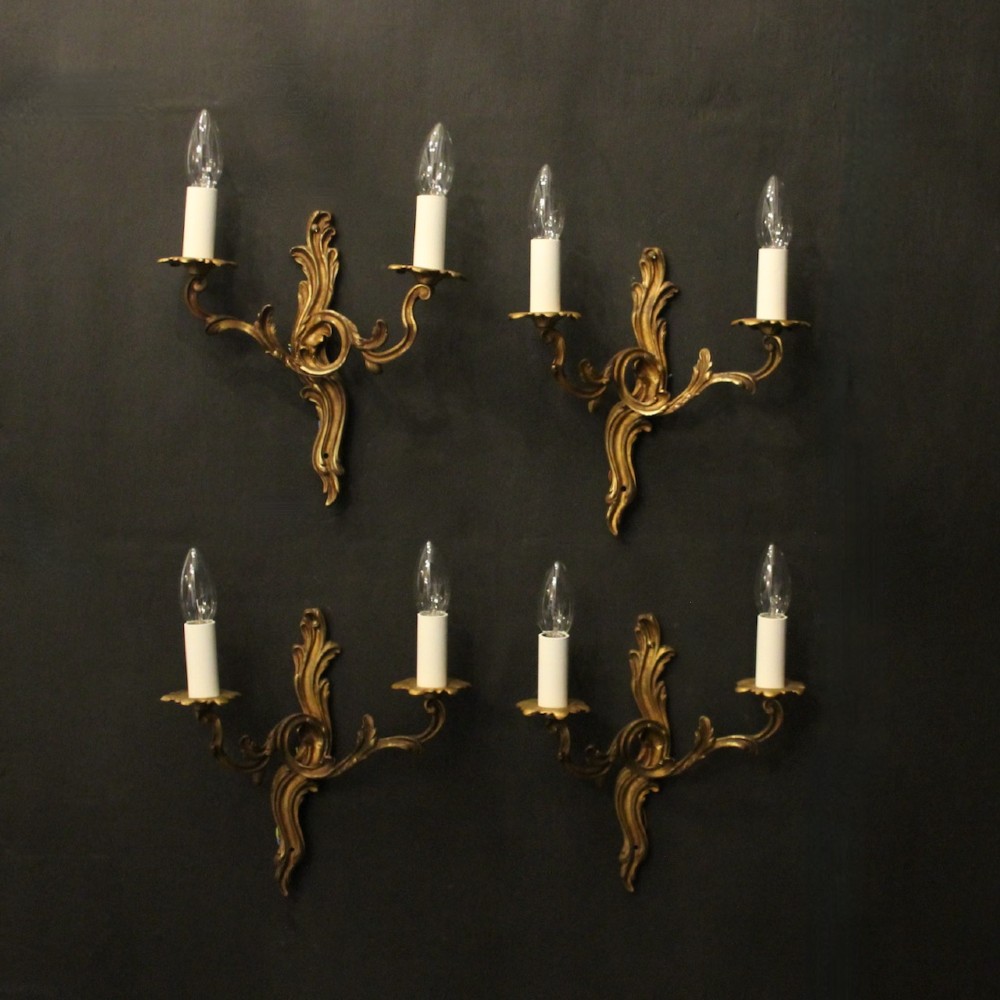 A set of four antique French twin-arm wall sconces crafted from gilded metal featuring ornate acanthus leaf scrolls.