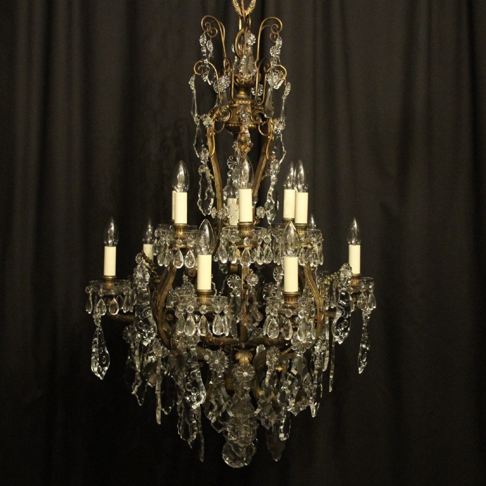 A French gilded bronze twelve-light chandelier featuring a scrollwork frame draped with faceted crystal drops and glass rosettes.