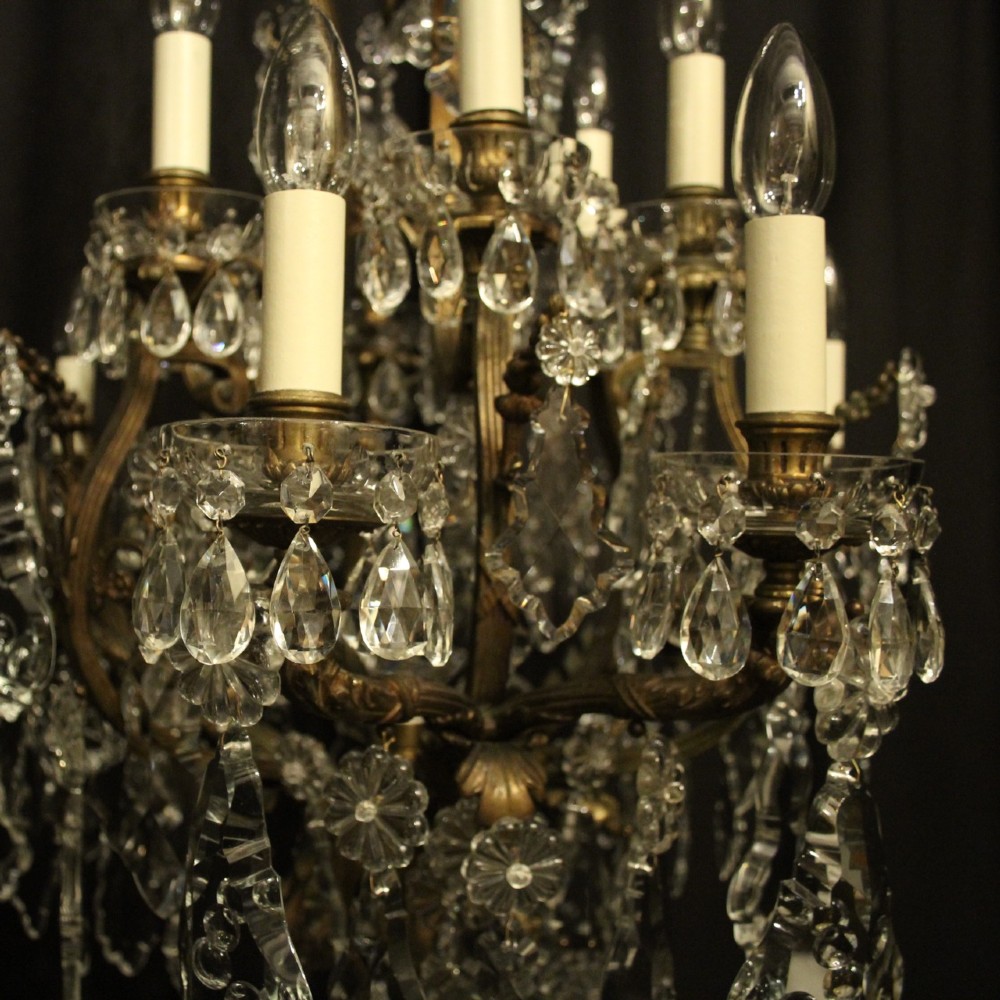 A French gilded bronze twelve-light chandelier featuring a scrollwork frame draped with faceted crystal drops and glass rosettes. View IV
