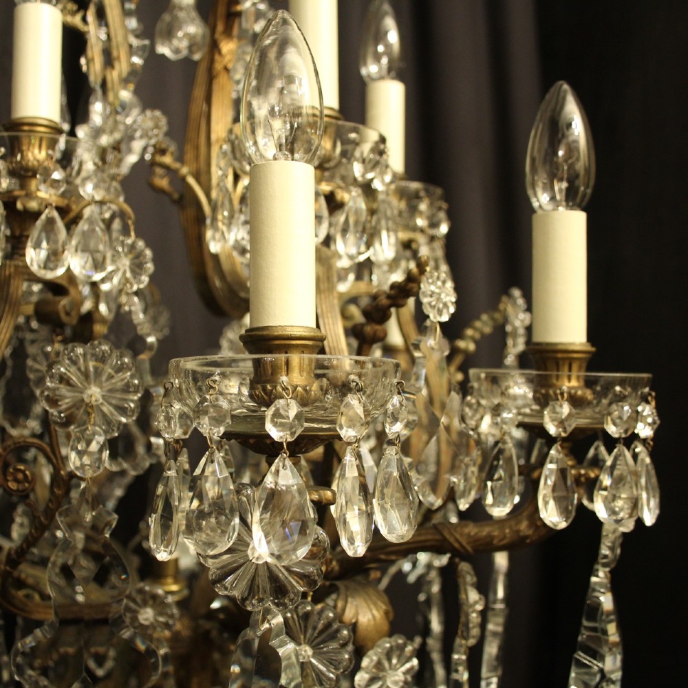 A French gilded bronze twelve-light chandelier featuring a scrollwork frame draped with faceted crystal drops and glass rosettes. View VI