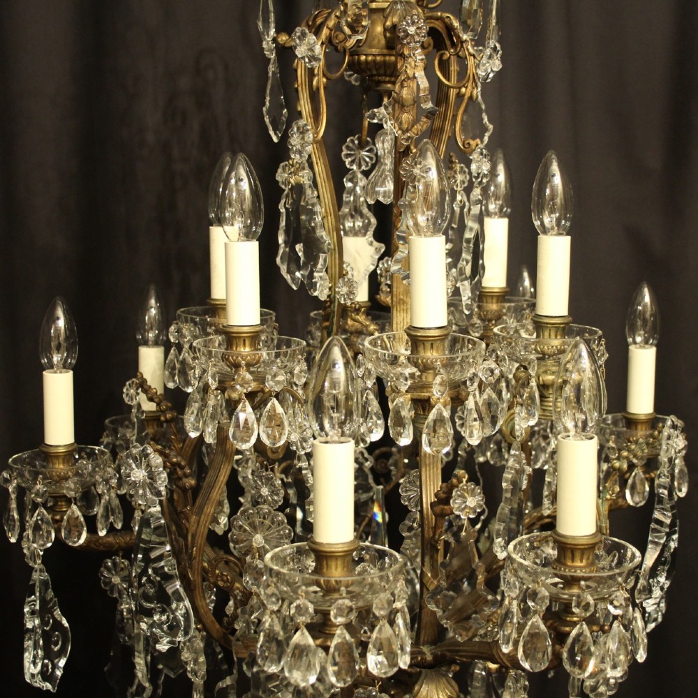 A French gilded bronze twelve-light chandelier featuring a scrollwork frame draped with faceted crystal drops and glass rosettes. View VII