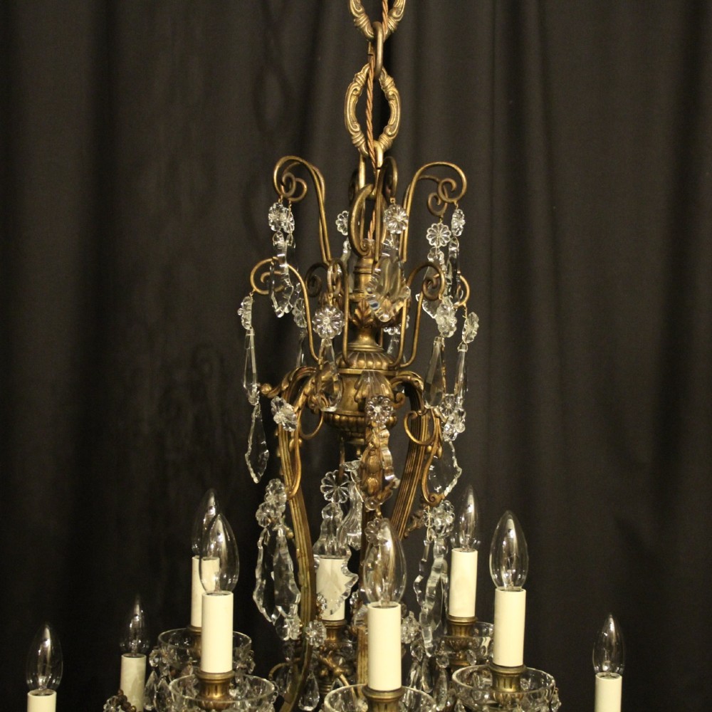 A French gilded bronze twelve-light chandelier featuring a scrollwork frame draped with faceted crystal drops and glass rosettes. View VIII