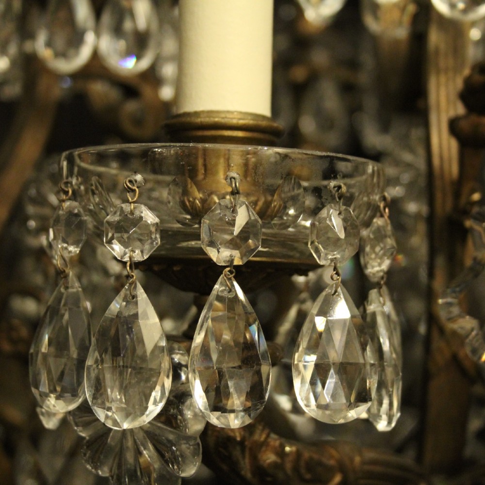 A French gilded bronze twelve-light chandelier featuring a scrollwork frame draped with faceted crystal drops and glass rosettes. View IX