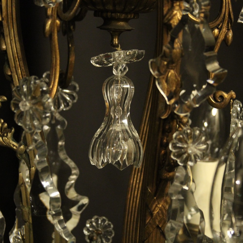 A French gilded bronze twelve-light chandelier featuring a scrollwork frame draped with faceted crystal drops and glass rosettes. View X