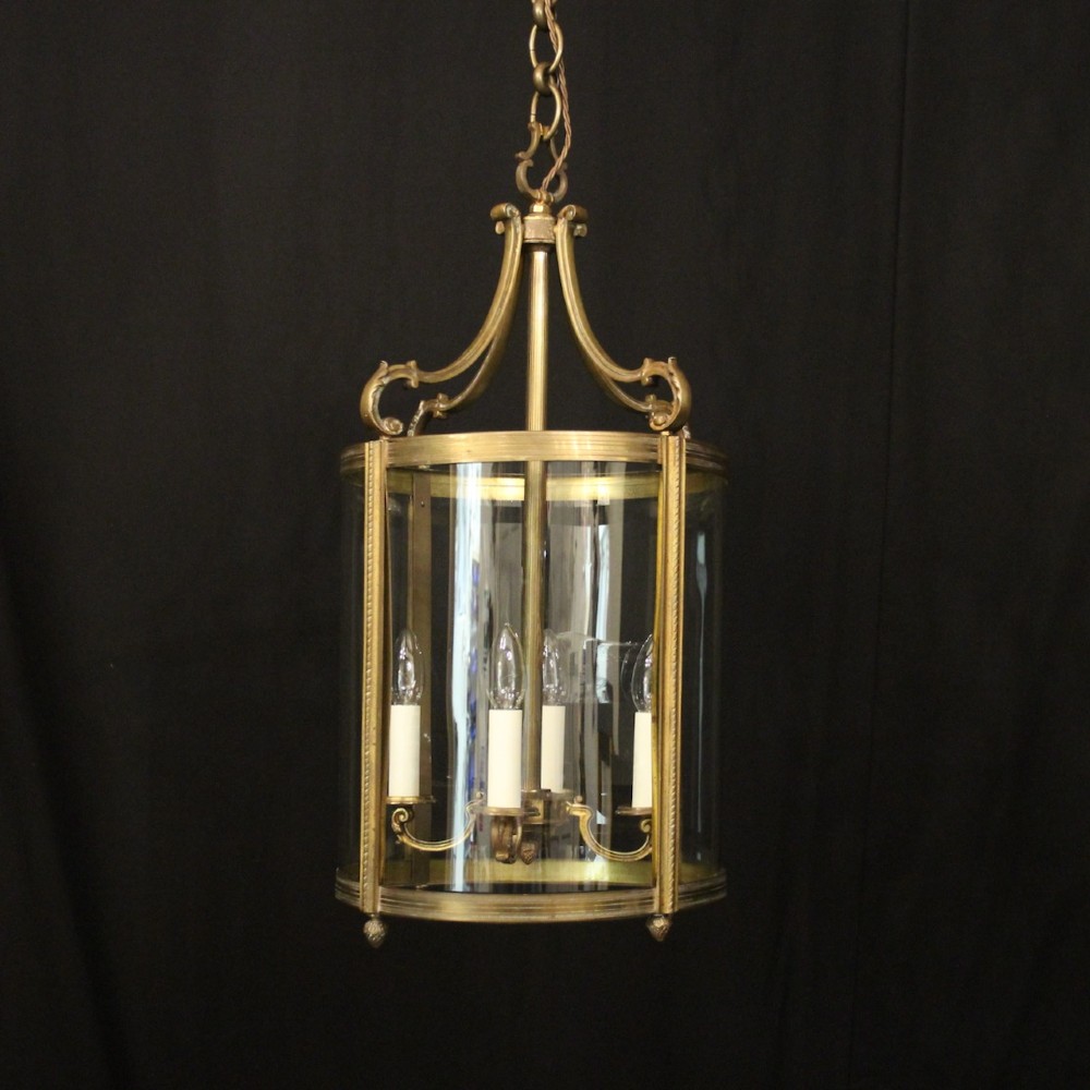 A cylindrical gilded bronze hall lantern with curved clear glass panels and four internal candle bulb fittings hanging from a chain.
