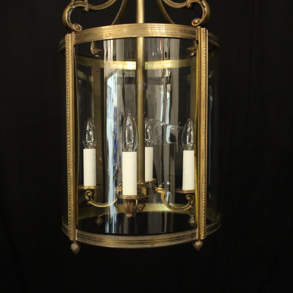 A cylindrical gilded bronze hall lantern with curved clear glass panels and four internal candle bulb fittings hanging from a chain. View III