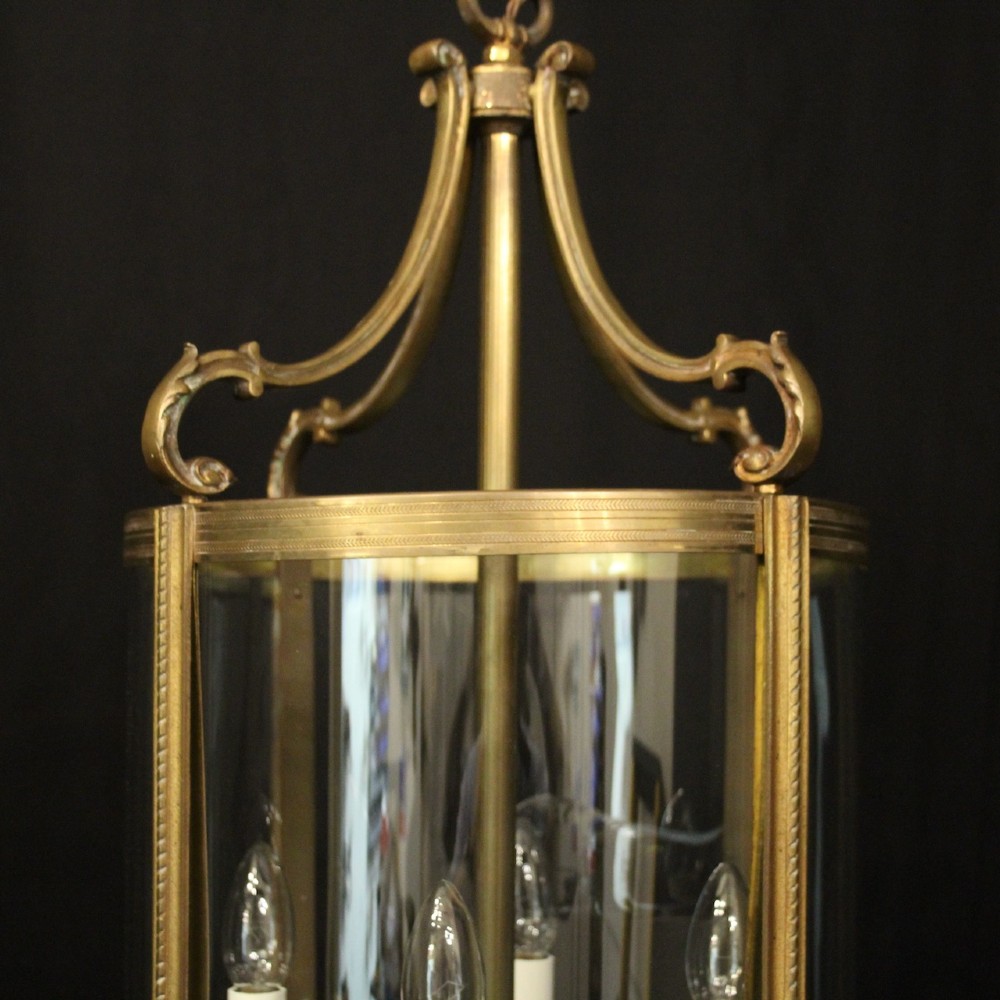 A cylindrical gilded bronze hall lantern with curved clear glass panels and four internal candle bulb fittings hanging from a chain. View IV