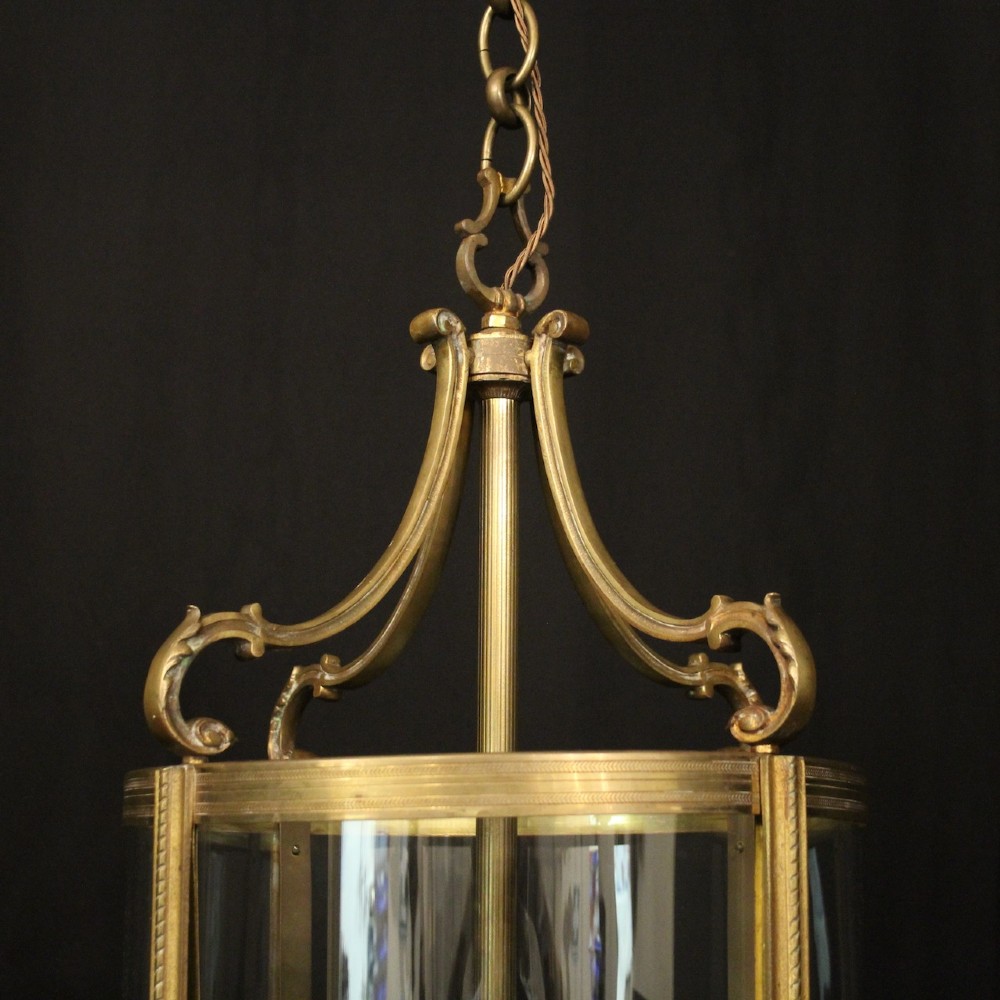 A cylindrical gilded bronze hall lantern with curved clear glass panels and four internal candle bulb fittings hanging from a chain. View V