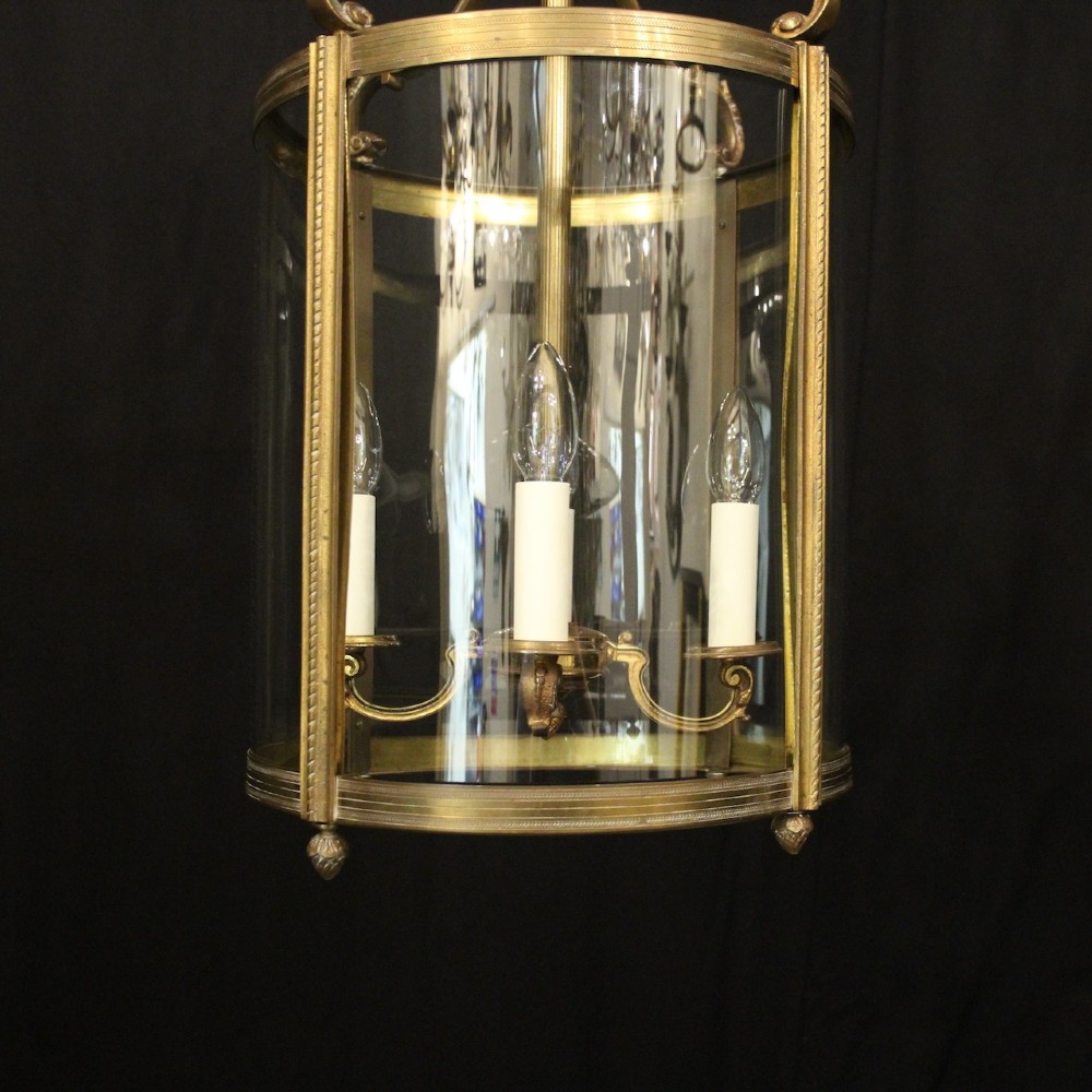A cylindrical gilded bronze hall lantern with curved clear glass panels and four internal candle bulb fittings hanging from a chain. View VI
