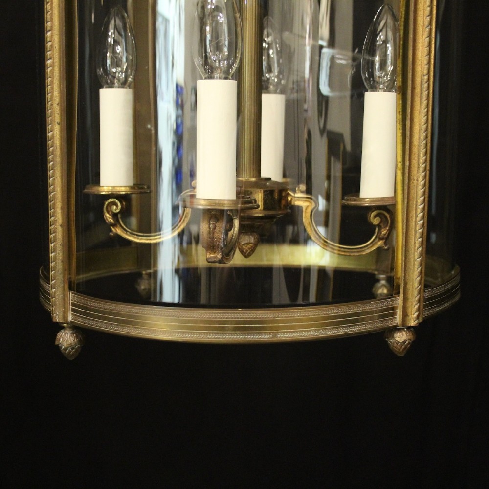 A cylindrical gilded bronze hall lantern with curved clear glass panels and four internal candle bulb fittings hanging from a chain. View VII