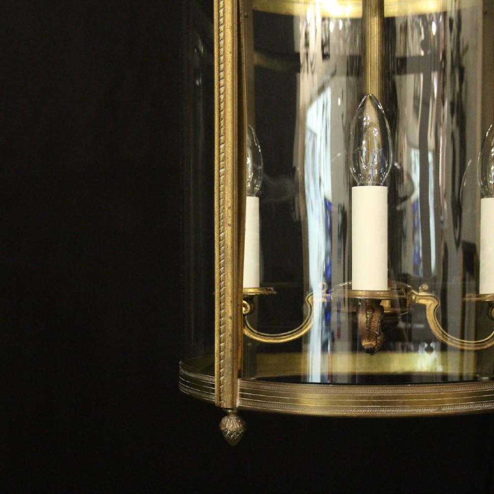A cylindrical gilded bronze hall lantern with curved clear glass panels and four internal candle bulb fittings hanging from a chain. View VIII