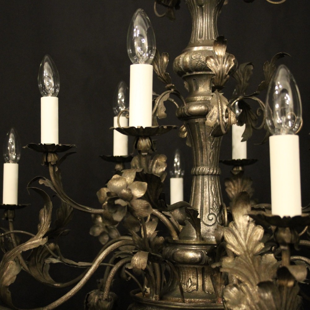 An antique Italian Genoa twelve-light chandelier crafted from gilded metal featuring ornate leaf motifs and scrolling arms supporting candle bulb holders. View V