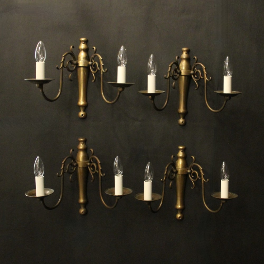 A set of four matching antique brass twin-arm wall sconces featuring curved scrollwork and candle-style bulb sockets.
