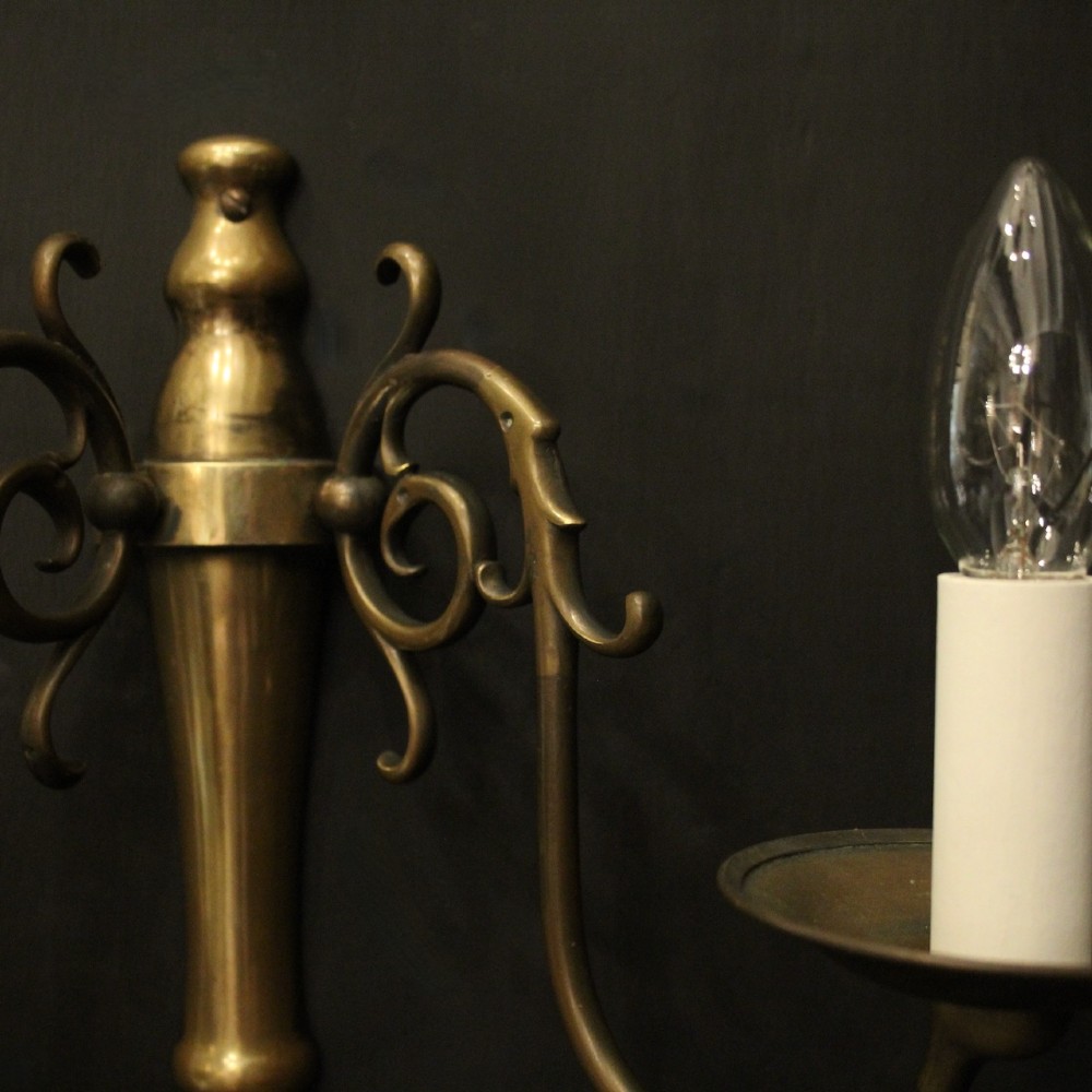 A set of four matching antique brass twin-arm wall sconces featuring curved scrollwork and candle-style bulb sockets. View VIII