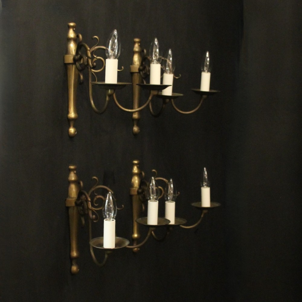 A set of four matching antique brass twin-arm wall sconces featuring curved scrollwork and candle-style bulb sockets. View X
