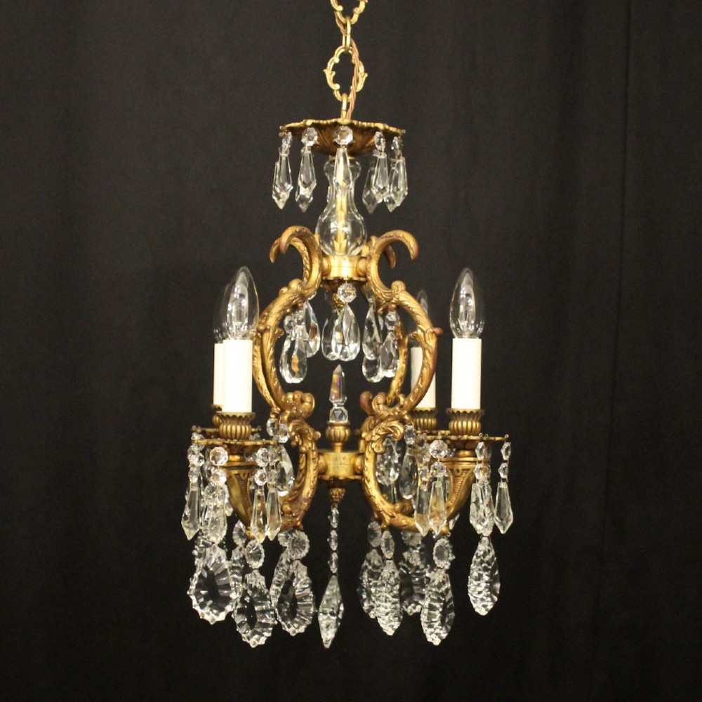 An antique French four-light chandelier featuring a scrollwork gilt bronze frame hung with faceted crystal drops.