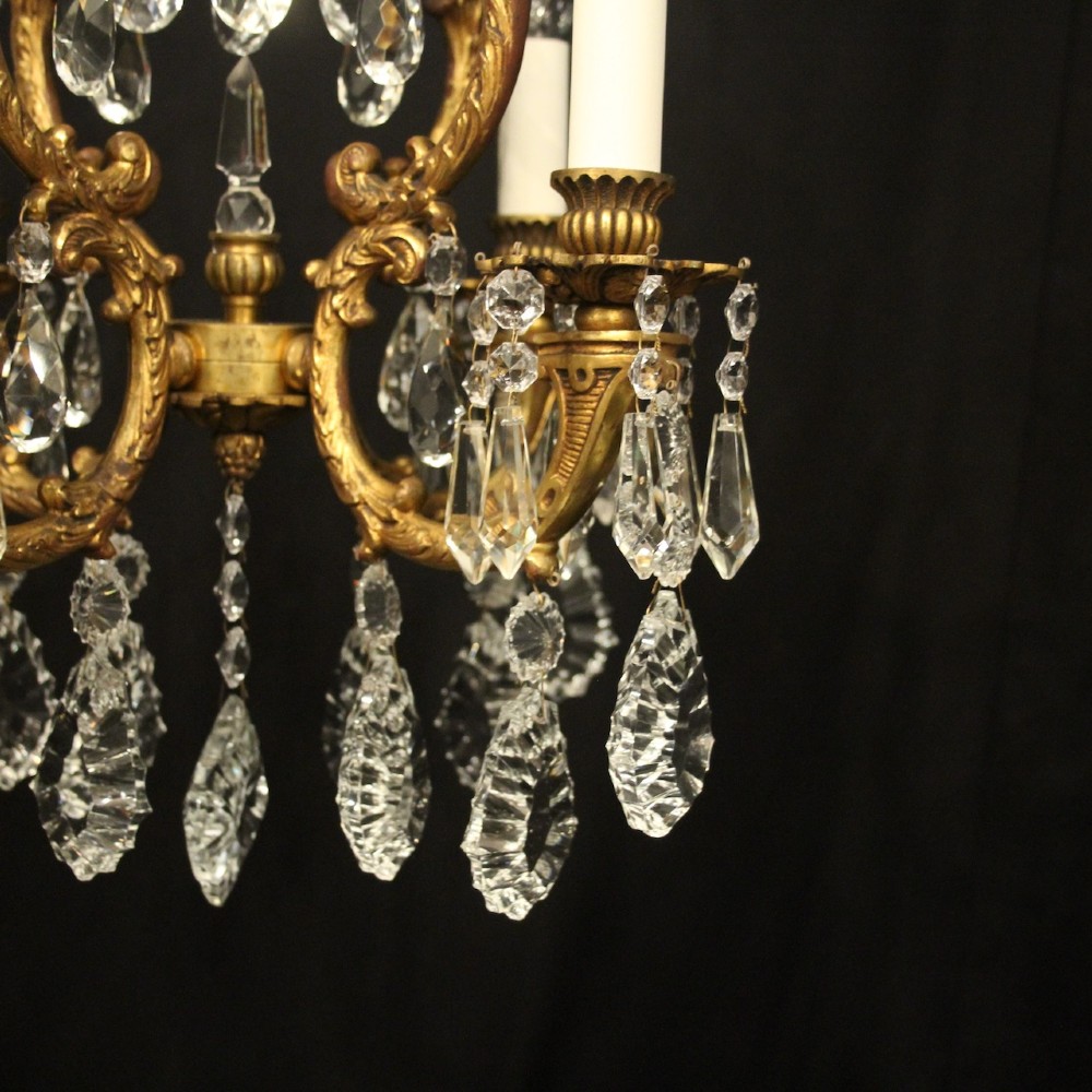 An antique French four-light chandelier featuring a scrollwork gilt bronze frame hung with faceted crystal drops. View V