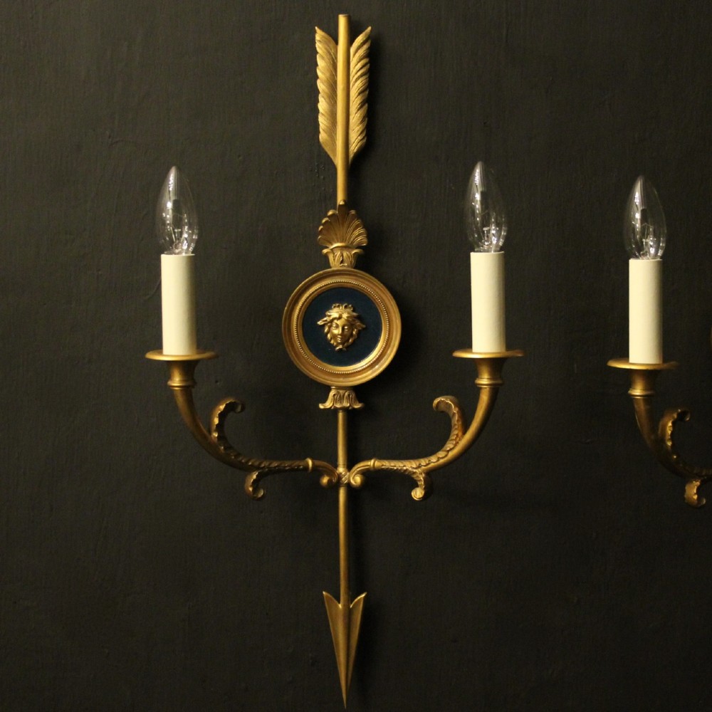 A pair of French gilt bronze twin-arm wall sconces featuring arrow-shaped backplates and central circular medallions with classical masks. View II