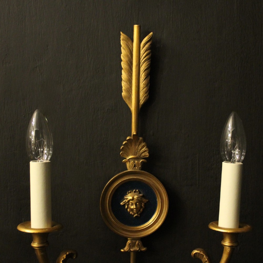 A pair of French gilt bronze twin-arm wall sconces featuring arrow-shaped backplates and central circular medallions with classical masks. View III