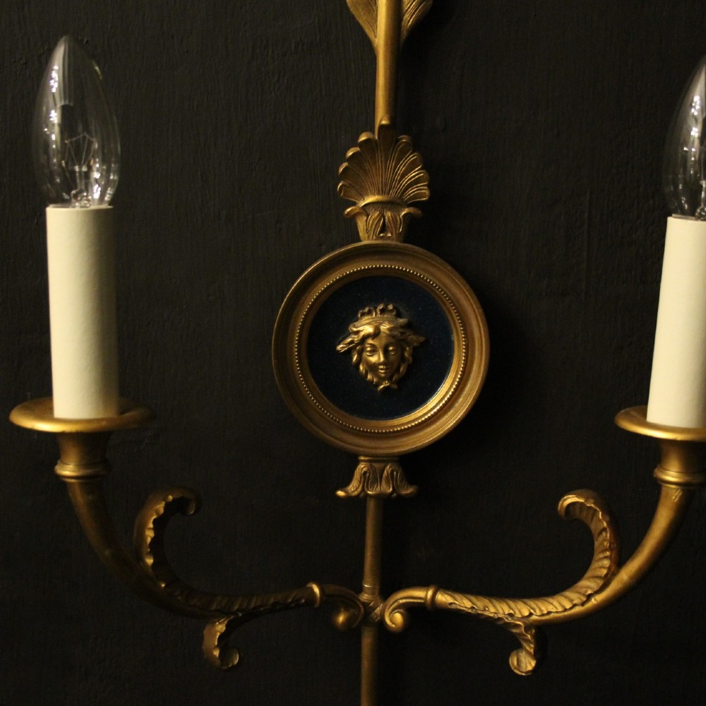 A pair of French gilt bronze twin-arm wall sconces featuring arrow-shaped backplates and central circular medallions with classical masks. View IV