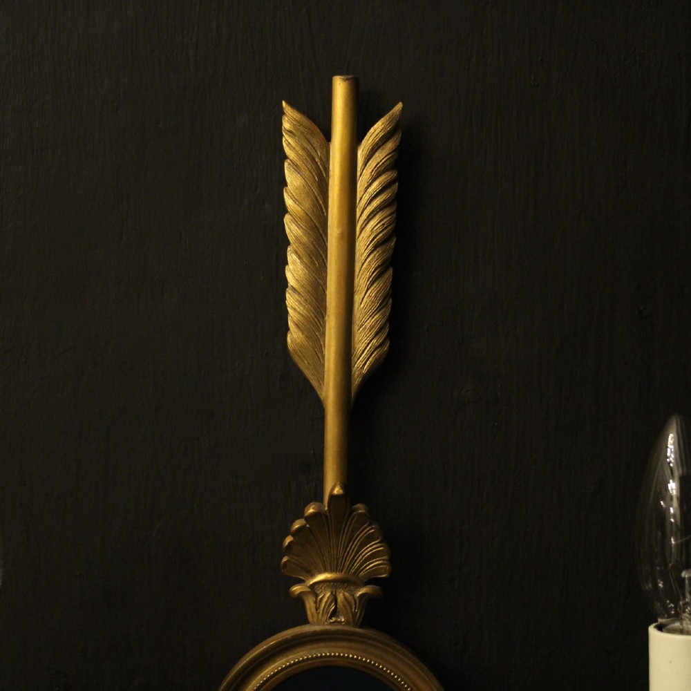 A pair of French gilt bronze twin-arm wall sconces featuring arrow-shaped backplates and central circular medallions with classical masks. View V