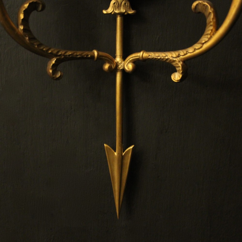 A pair of French gilt bronze twin-arm wall sconces featuring arrow-shaped backplates and central circular medallions with classical masks. View VII
