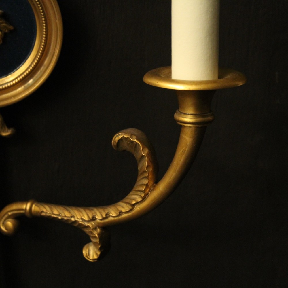 A pair of French gilt bronze twin-arm wall sconces featuring arrow-shaped backplates and central circular medallions with classical masks. View VIII
