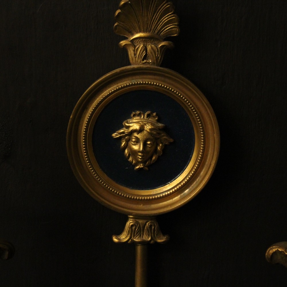 A pair of French gilt bronze twin-arm wall sconces featuring arrow-shaped backplates and central circular medallions with classical masks. View IX