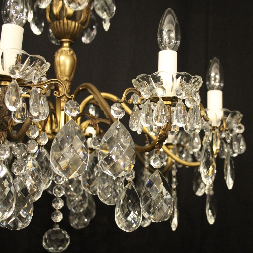 An eight-arm gilded metal chandelier suspended from a chain, decorated with faceted glass droplets and glass candle-style light holders. View II