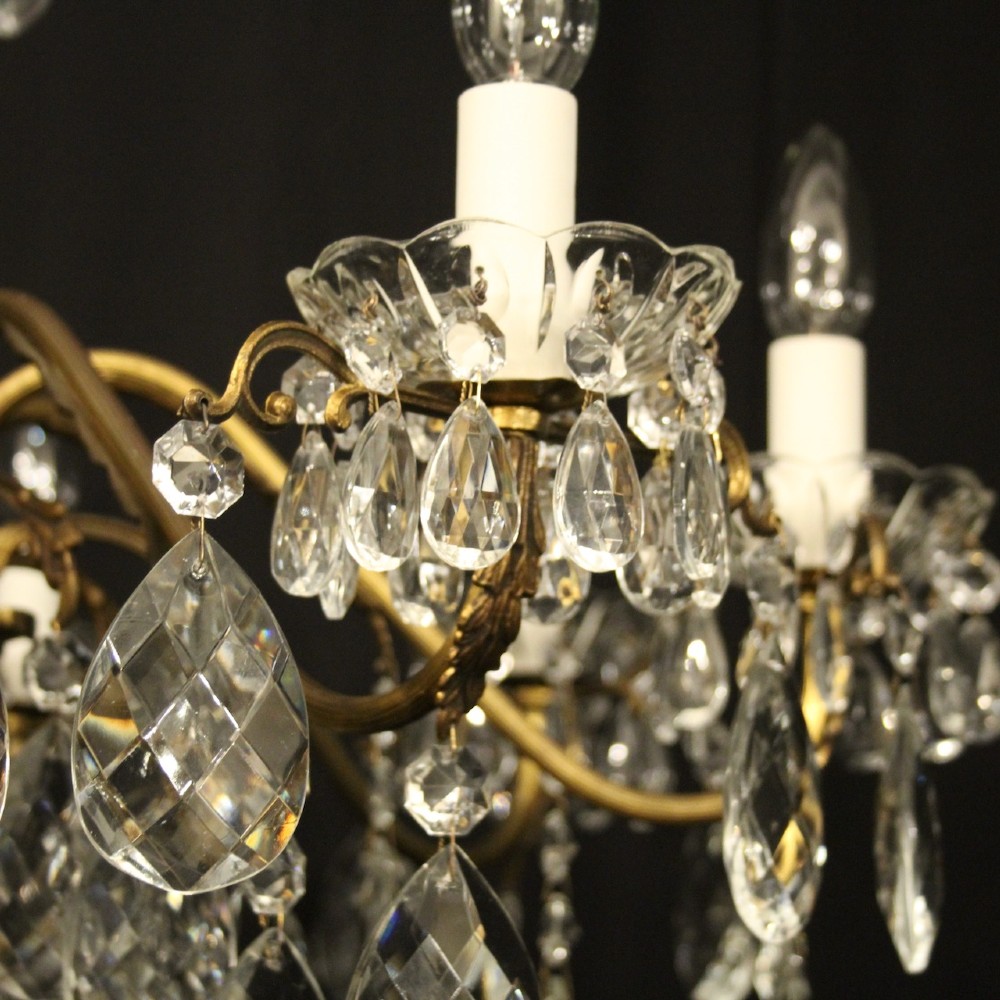 An eight-arm gilded metal chandelier suspended from a chain, decorated with faceted glass droplets and glass candle-style light holders. View III