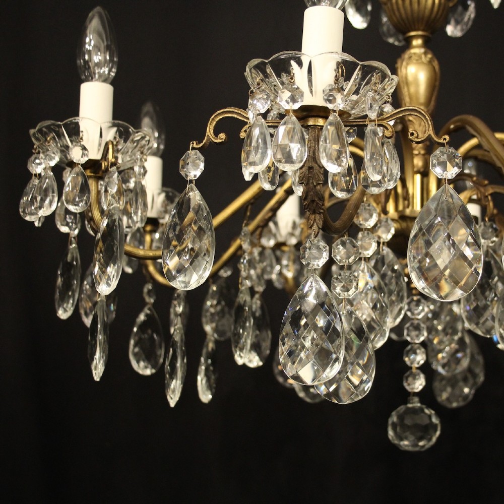 An eight-arm gilded metal chandelier suspended from a chain, decorated with faceted glass droplets and glass candle-style light holders. View IV