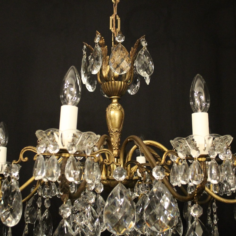 An eight-arm gilded metal chandelier suspended from a chain, decorated with faceted glass droplets and glass candle-style light holders. View V