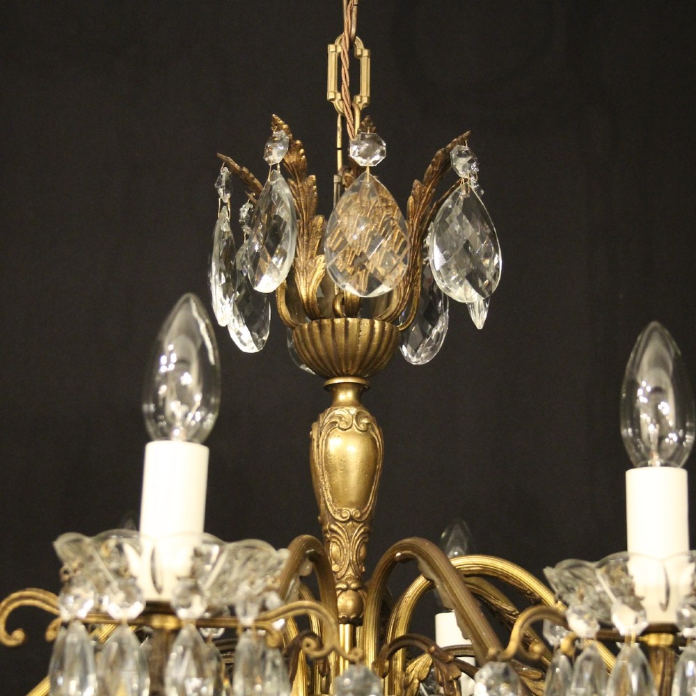 An eight-arm gilded metal chandelier suspended from a chain, decorated with faceted glass droplets and glass candle-style light holders. View VI