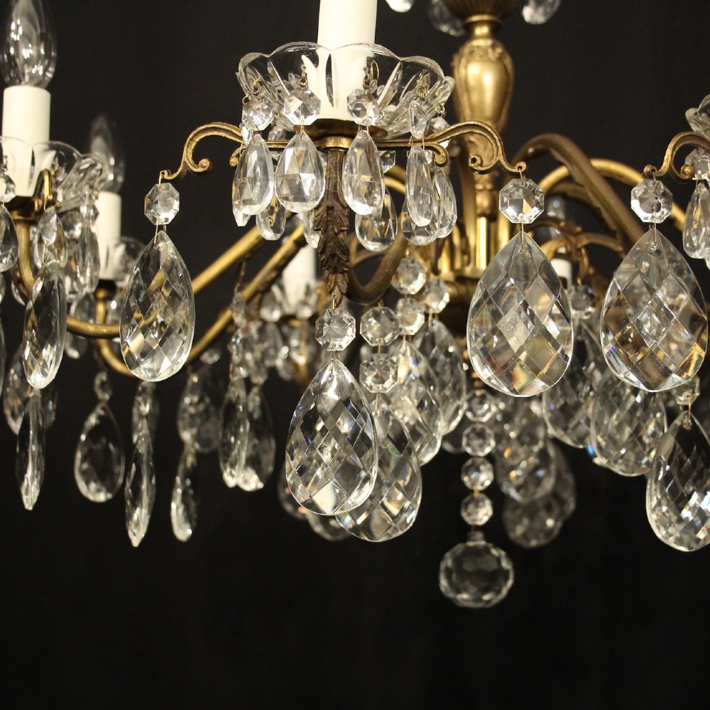 An eight-arm gilded metal chandelier suspended from a chain, decorated with faceted glass droplets and glass candle-style light holders. View IX