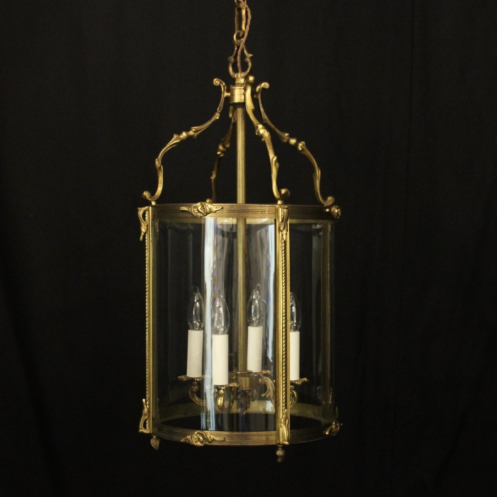 An antique French gilded bronze hall lantern featuring convex glass panels surrounding a four-light candle-style fixture with ornate scrollwork top brackets.