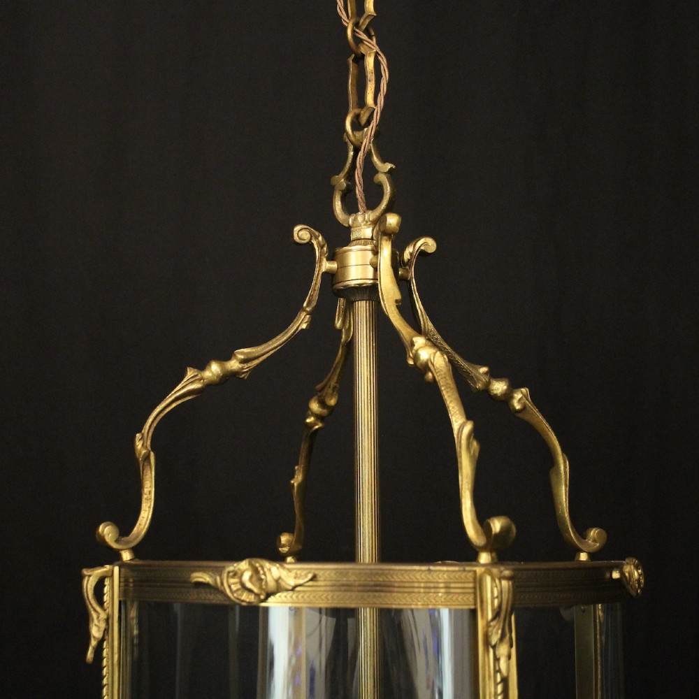 An antique French gilded bronze hall lantern featuring convex glass panels surrounding a four-light candle-style fixture with ornate scrollwork top brackets. View IV