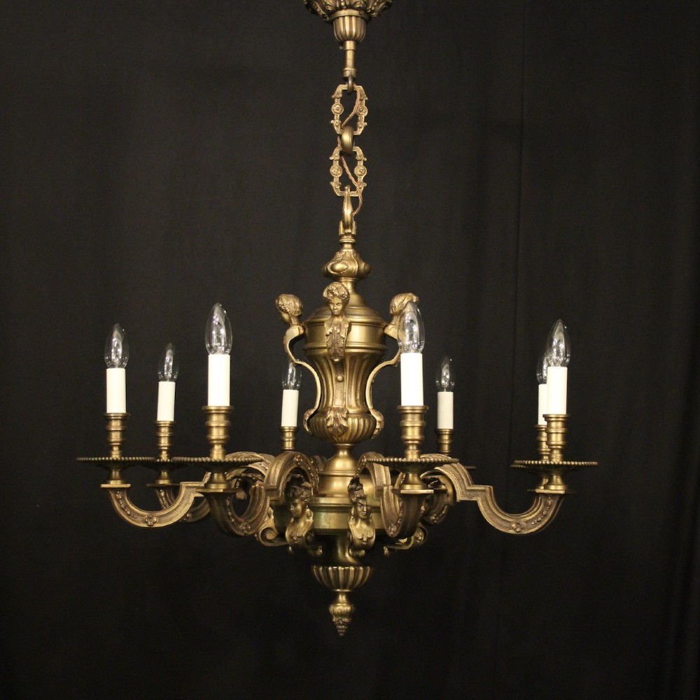 An eight-arm French gilt bronze chandelier featuring an urn-shaped central stem, cast classical busts, and candle-style bulb holders.