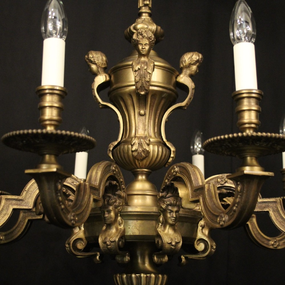 An eight-arm French gilt bronze chandelier featuring an urn-shaped central stem, cast classical busts, and candle-style bulb holders. View VI