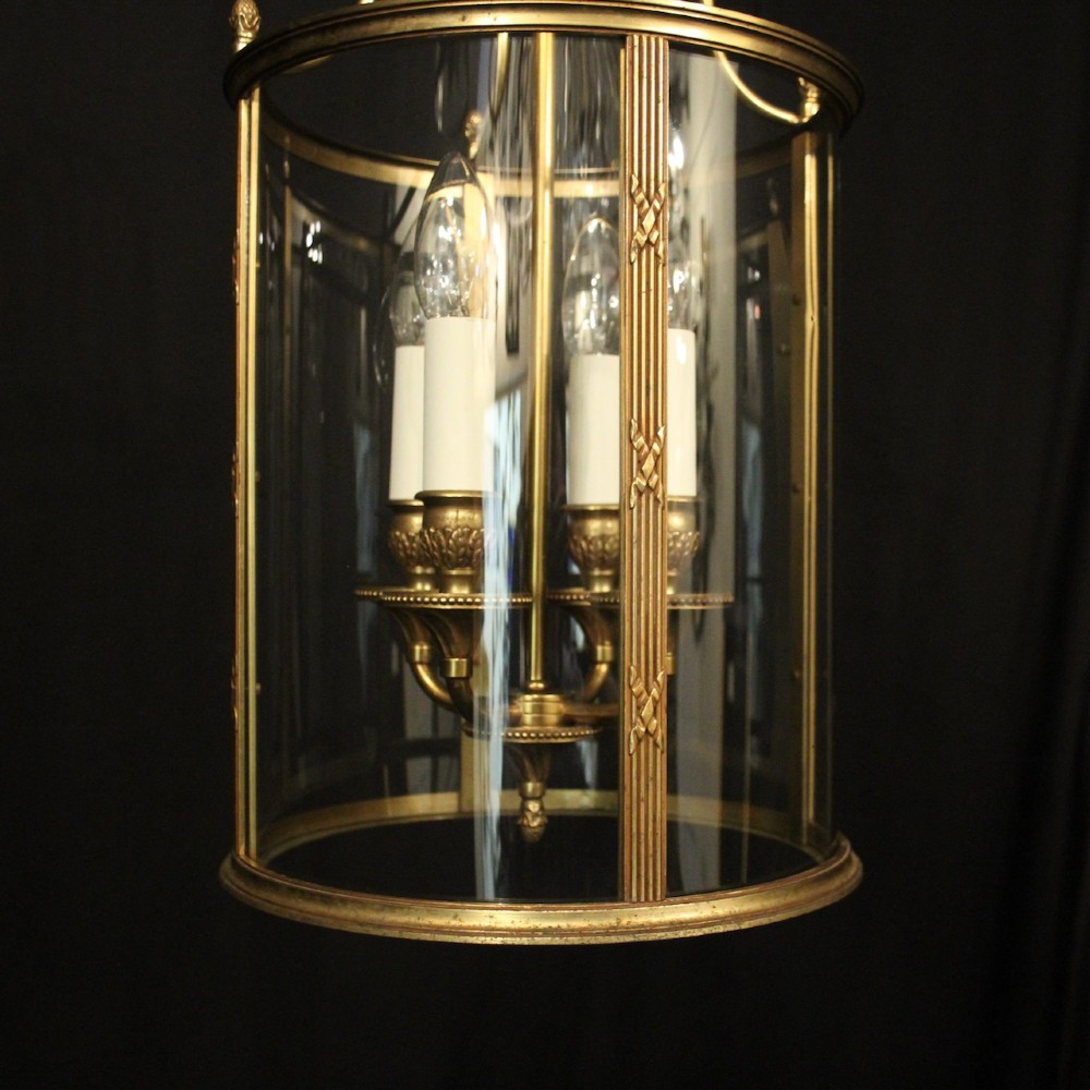 A cylindrical French gilded bronze hall lantern featuring curved glass panels and four internal candle-style light fittings. View IV