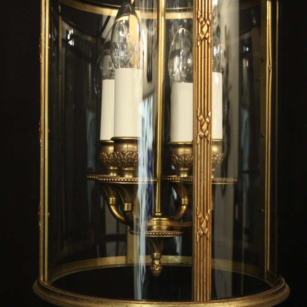 A cylindrical French gilded bronze hall lantern featuring curved glass panels and four internal candle-style light fittings. View VIII