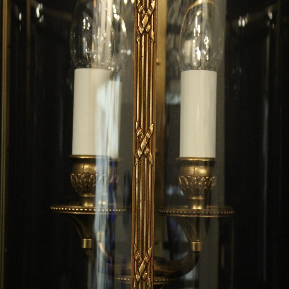A cylindrical French gilded bronze hall lantern featuring curved glass panels and four internal candle-style light fittings. View IX