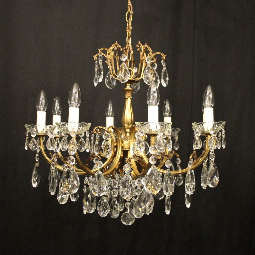 An eight-light French gilded brass chandelier featuring decorative scroll arms and hanging faceted crystal drops.