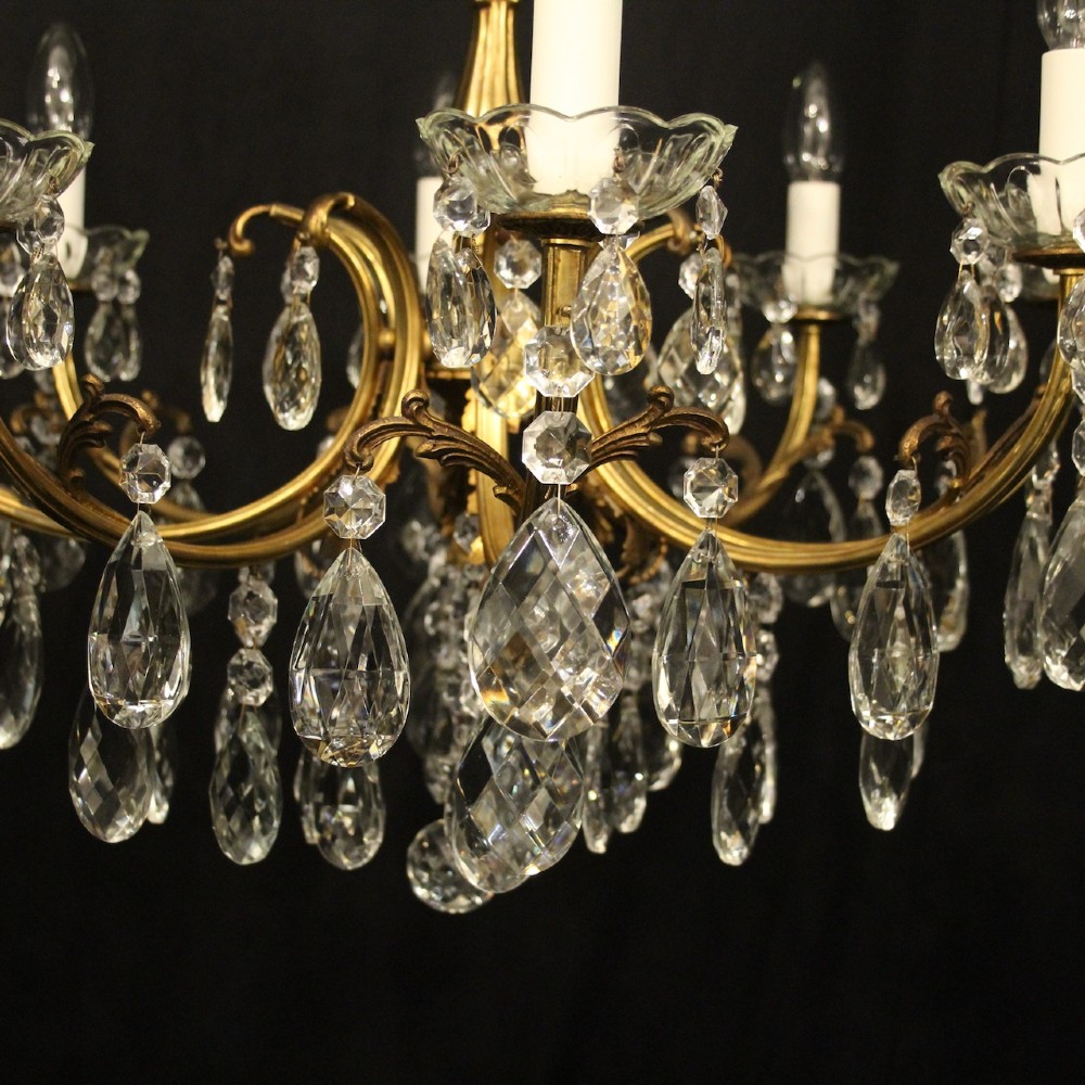 An eight-light French gilded brass chandelier featuring decorative scroll arms and hanging faceted crystal drops. View VI