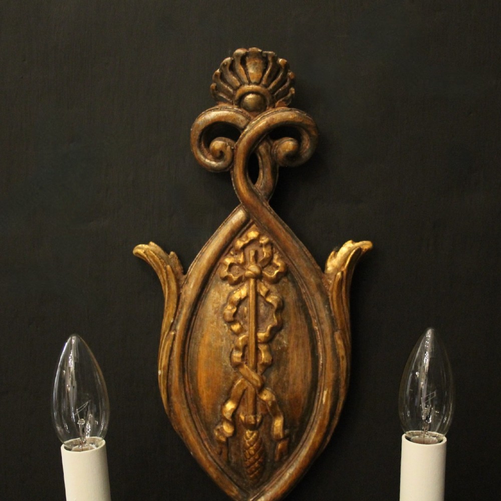 A pair of Florentine carved giltwood twin arm wall lights featuring ribbon and scroll motifs with white candle sleeves. View IV