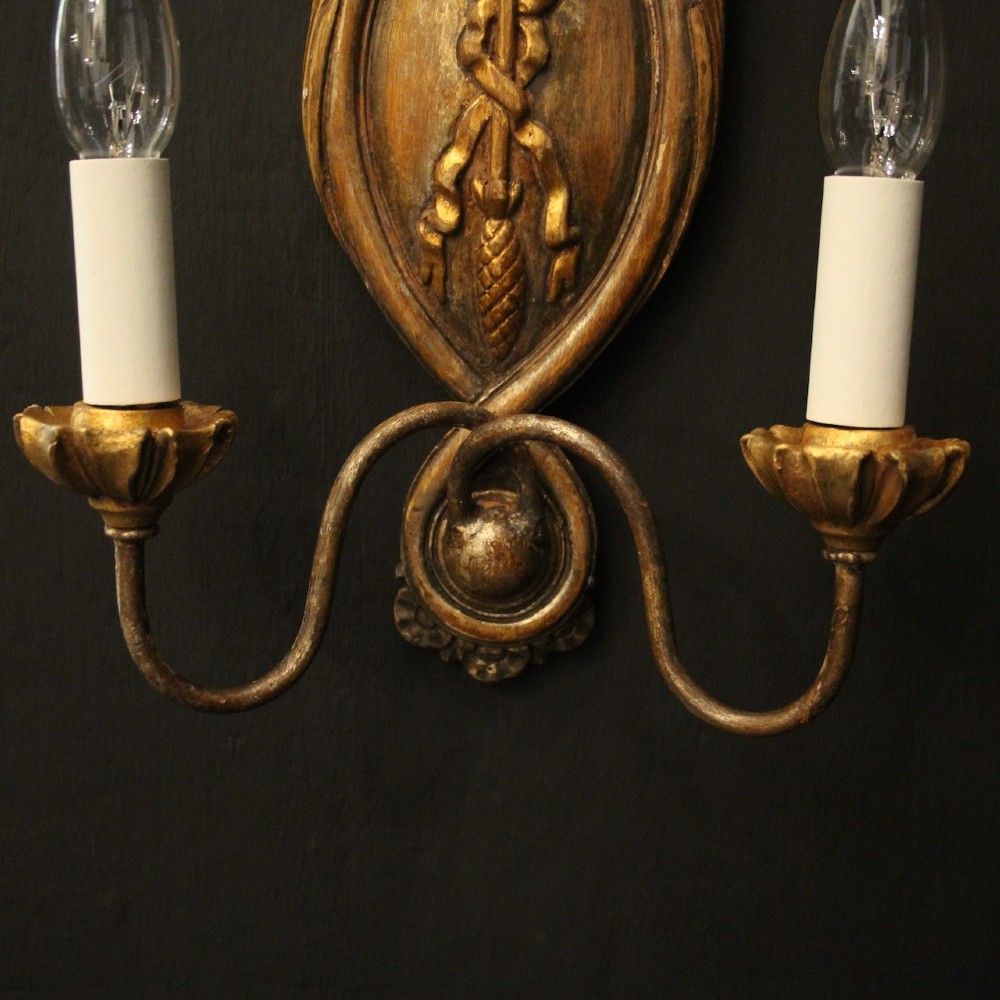 A pair of Florentine carved giltwood twin arm wall lights featuring ribbon and scroll motifs with white candle sleeves. View IX