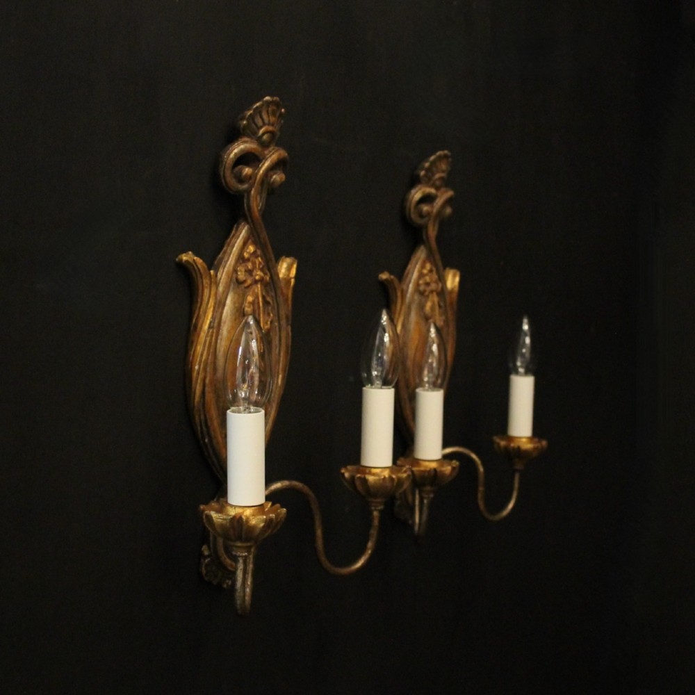 A pair of Florentine carved giltwood twin arm wall lights featuring ribbon and scroll motifs with white candle sleeves. View X